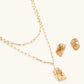 Sculptural gold-toned jewelry set with organic fluid shapes including earrings and layered chain necklace on cream background.